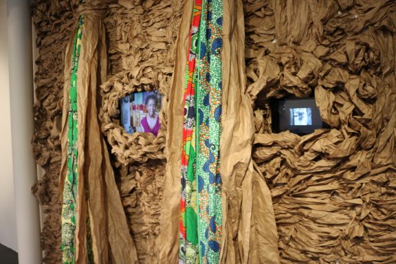Close-up view of textured wall installation with colorful fabric and video monitors embedded.