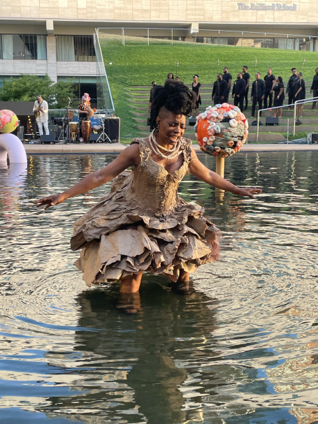 A woman in a flowing dress stands in water, performing playfully with a colorful ball.