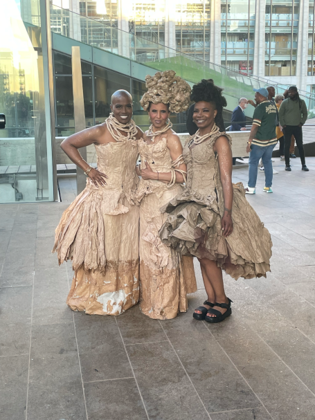 Three women dressed in elaborate, glamorous golden gowns with unique hairstyles.