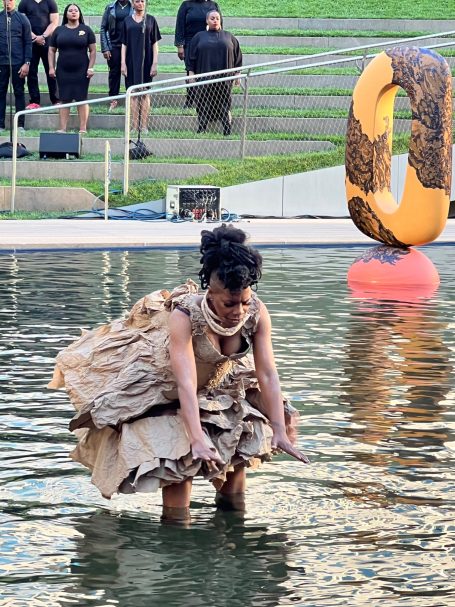 A performer in a flowing dress wades through water during an outdoor event.