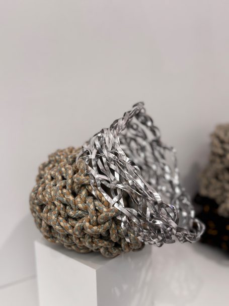 A textured sculpture featuring intertwined gray and metallic elements.