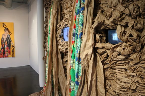 Partial view of textured wall installation with colorful fabric and video monitors embedded.