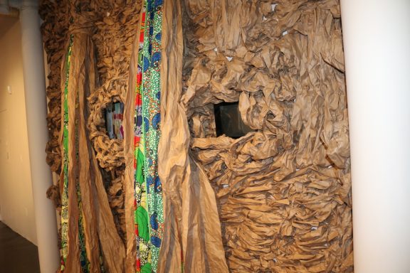 Close-up view of textured wall installation with colorful fabric and video monitors embedded.
