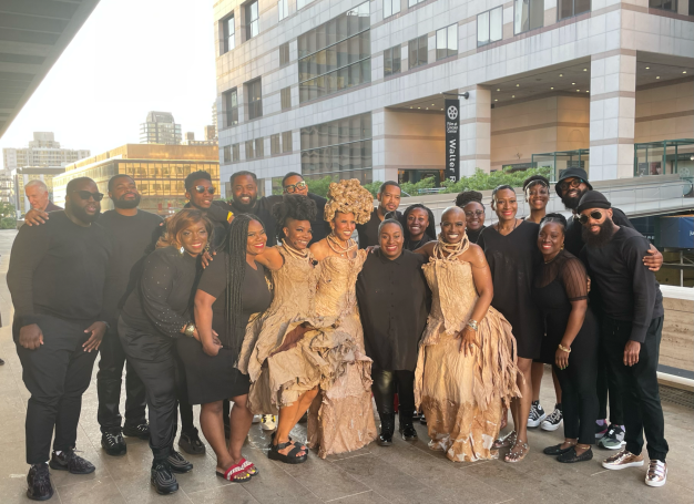 A diverse group of people poses together, dressed in elegant attire and casual black outfits.
