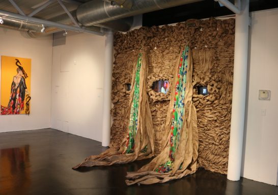 Art installation featuring textured wall with colorful elements and fabric drapes.