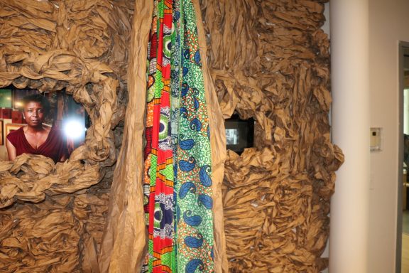 Textured wall art featuring colorful fabric draped and framed photos embedded within.