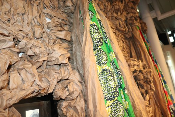 Textured wall made of crumpled paper and vibrant patterned fabric draped alongside it.