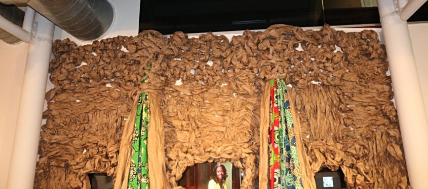 Close-up view of textured wall installation with colorful fabric and video monitors embedded.