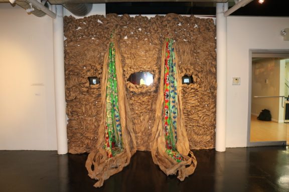View of textured wall installation with colorful fabric and video monitors embedded.